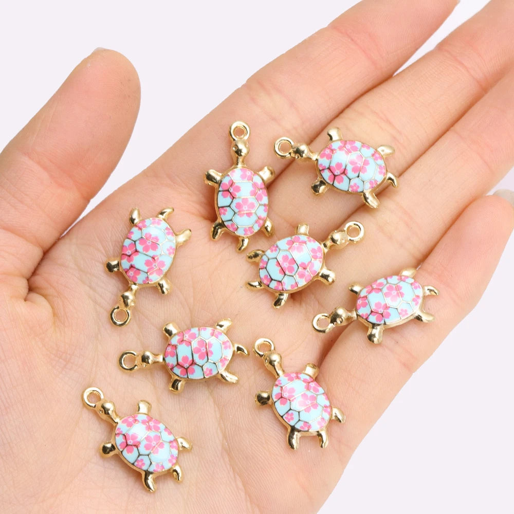 Gold-tone 24mm turtle charms with pink and turquoise flower shells held in a palm