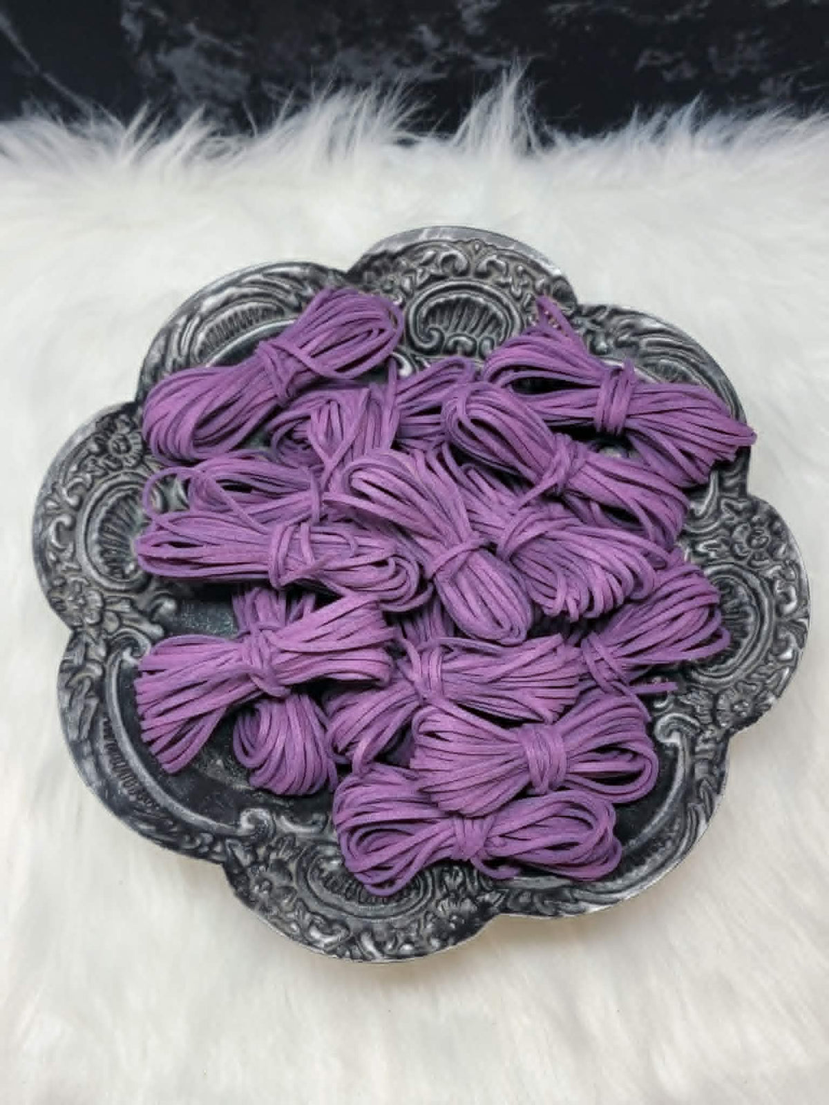Bundles of 2.7mm plum suede leather lacing coiled on a dark scalloped dish