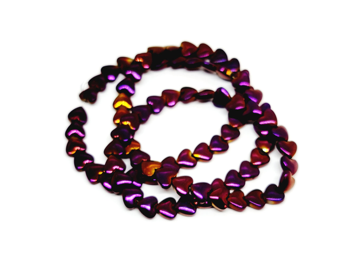 Strand of 6mm purple rainbow hematite heart beads coiled on a white background