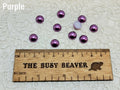 Ten 10mm purple pearl-look resin half round cabochons (cabs) beside a ruler