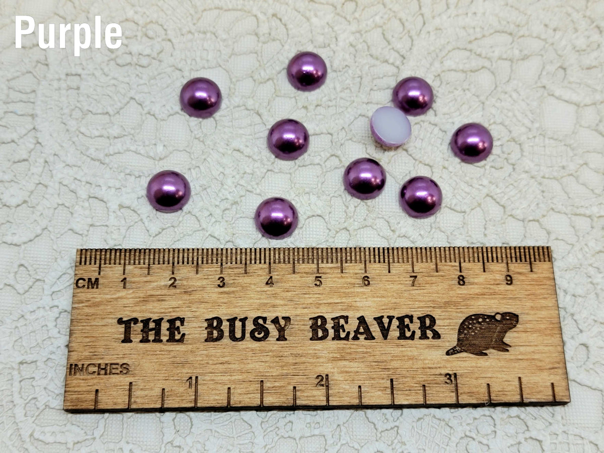 Ten 10mm purple pearl-look resin half round cabochons (cabs) beside a ruler