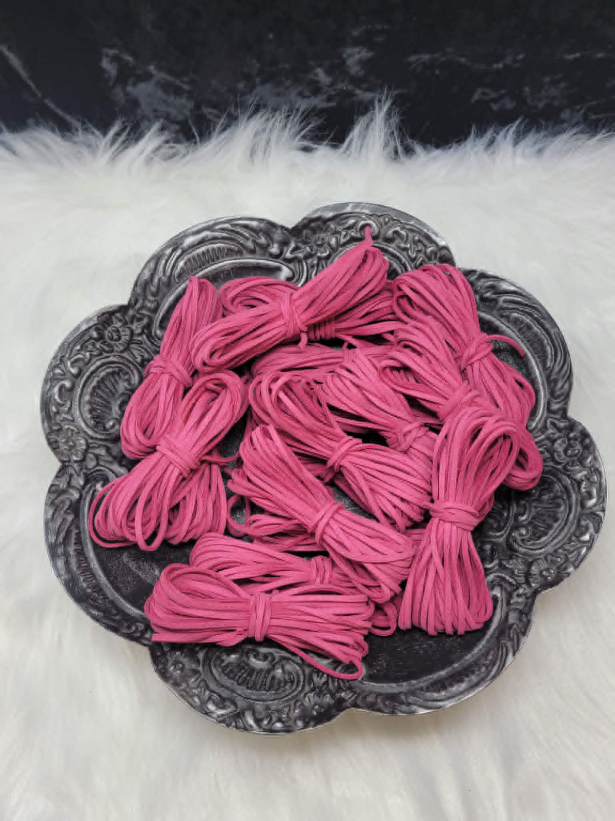 Bundles of 2.7mm raspberry suede leather lacing coiled on a dark scalloped dish