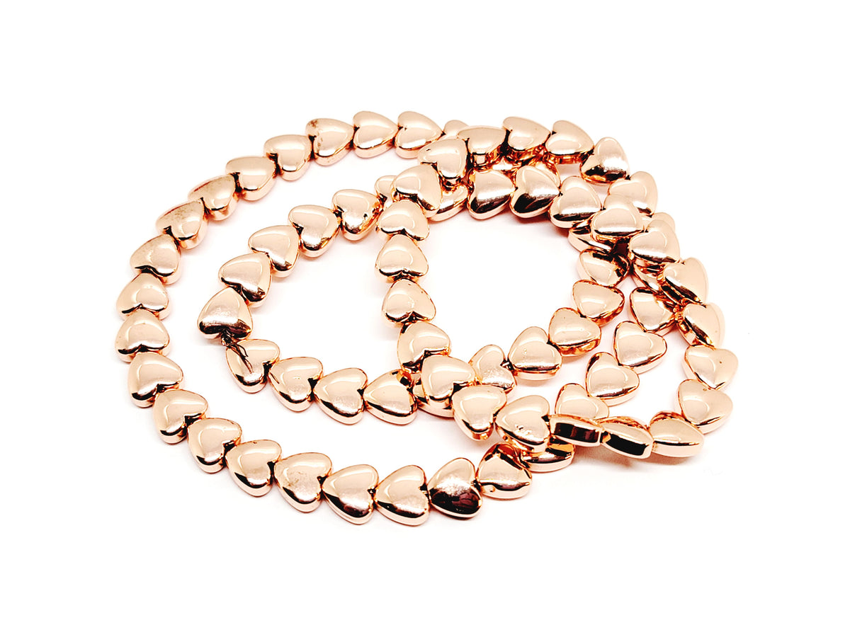 Strand of 6mm rose gold hematite heart beads coiled on a white background