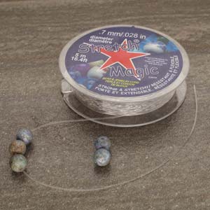 Stretch Magic clear cord spool with cord unwound and stone beads strung on it
