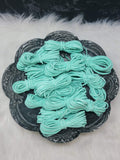 Bundles of 2.7mm seafoam suede leather lacing coiled on a dark scalloped dish
