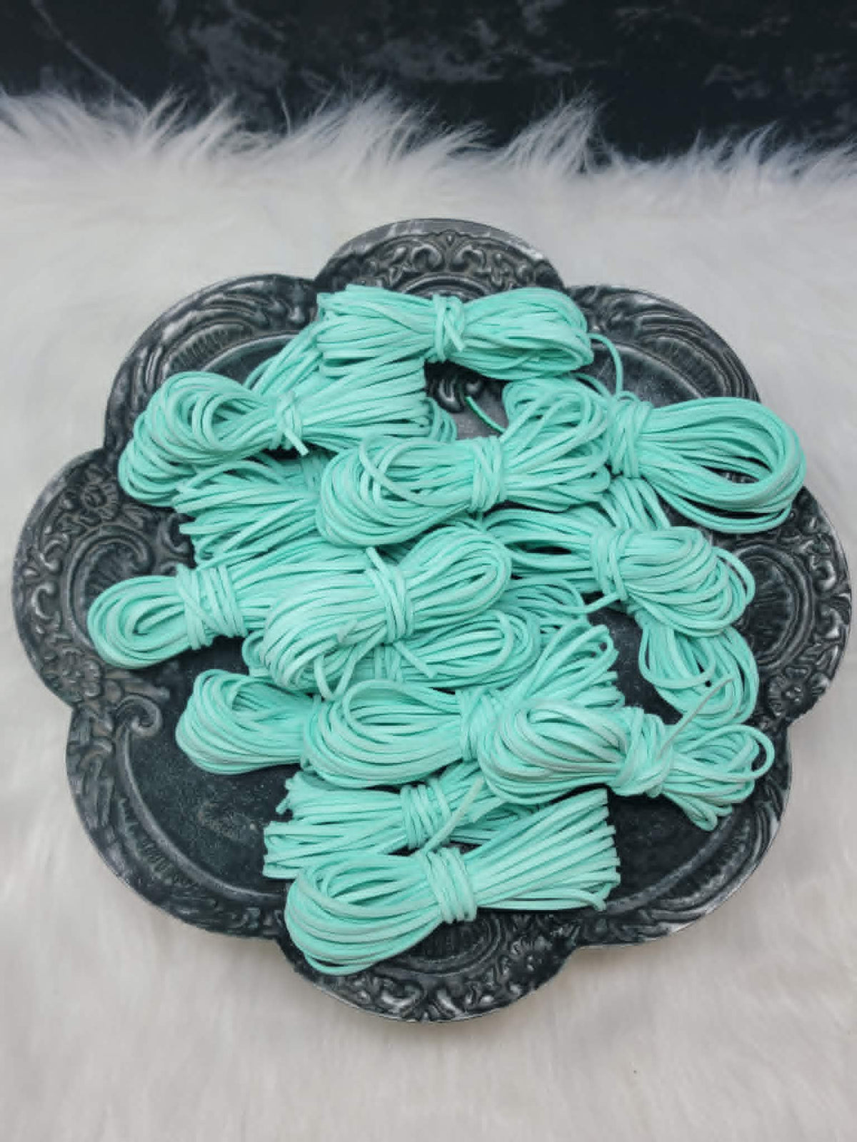 Bundles of 2.7mm seafoam suede leather lacing coiled on a dark scalloped dish
