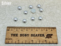 Ten 10mm silver pearl-look resin half round cabochons (cabs) beside a ruler