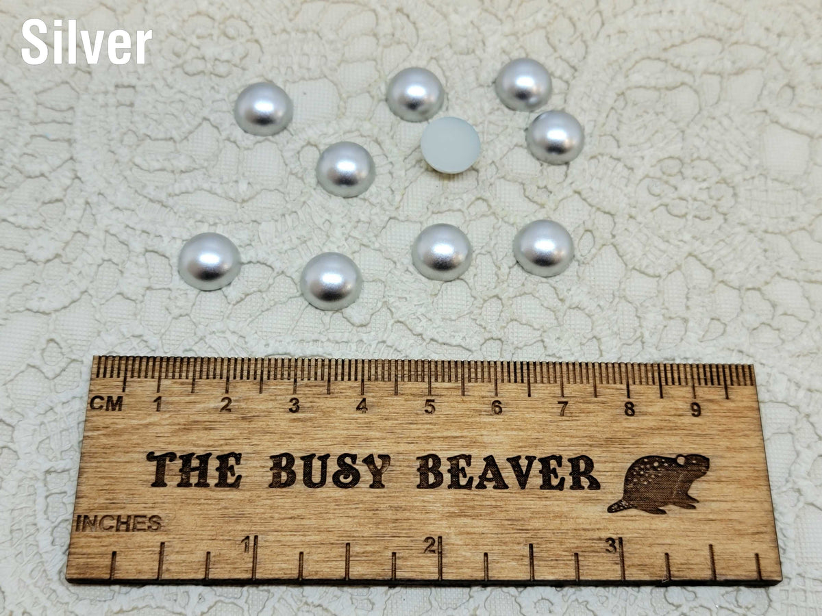 Ten 10mm silver pearl-look resin half round cabochons (cabs) beside a ruler