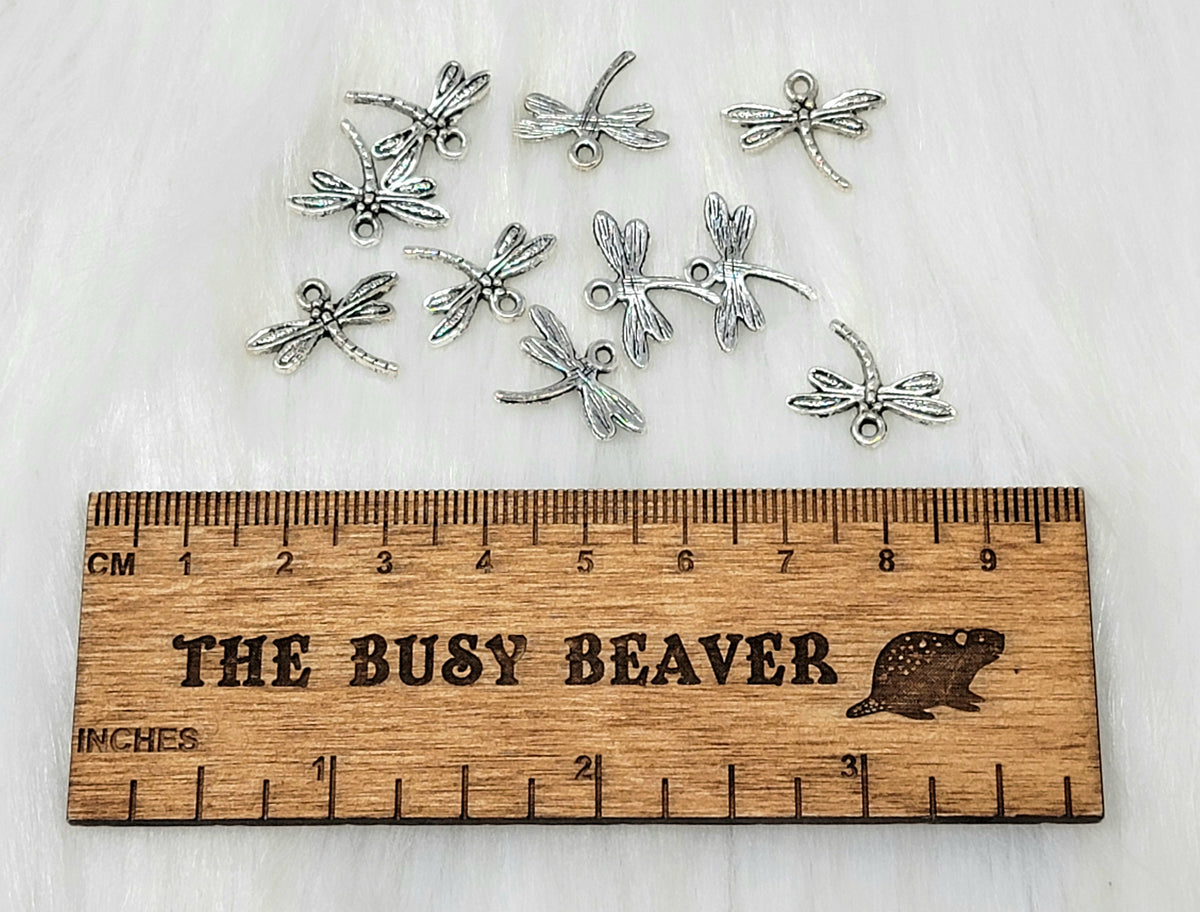 Ten silver-tone 18 x 15mm dragonfly charms beside a ruler for scale