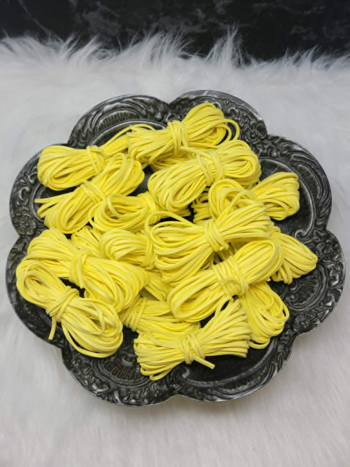 Bundles of 2.7mm sunshine yellow suede leather lacing coiled on a dark scalloped dish