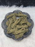 Bundles of 2.7mm sweet grass suede leather lacing coiled on a dark scalloped dish