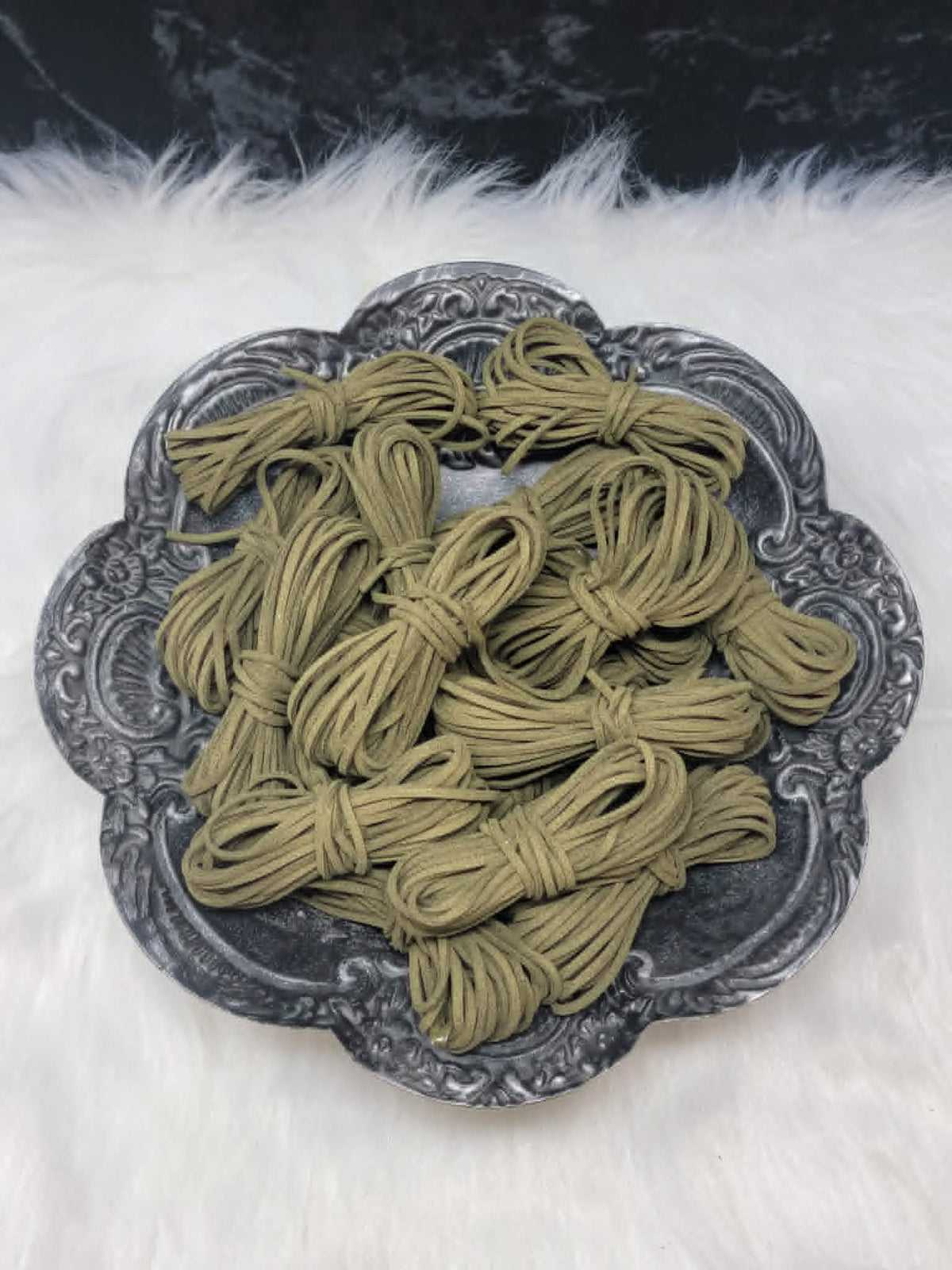 Bundles of 2.7mm sweet grass suede leather lacing coiled on a dark scalloped dish