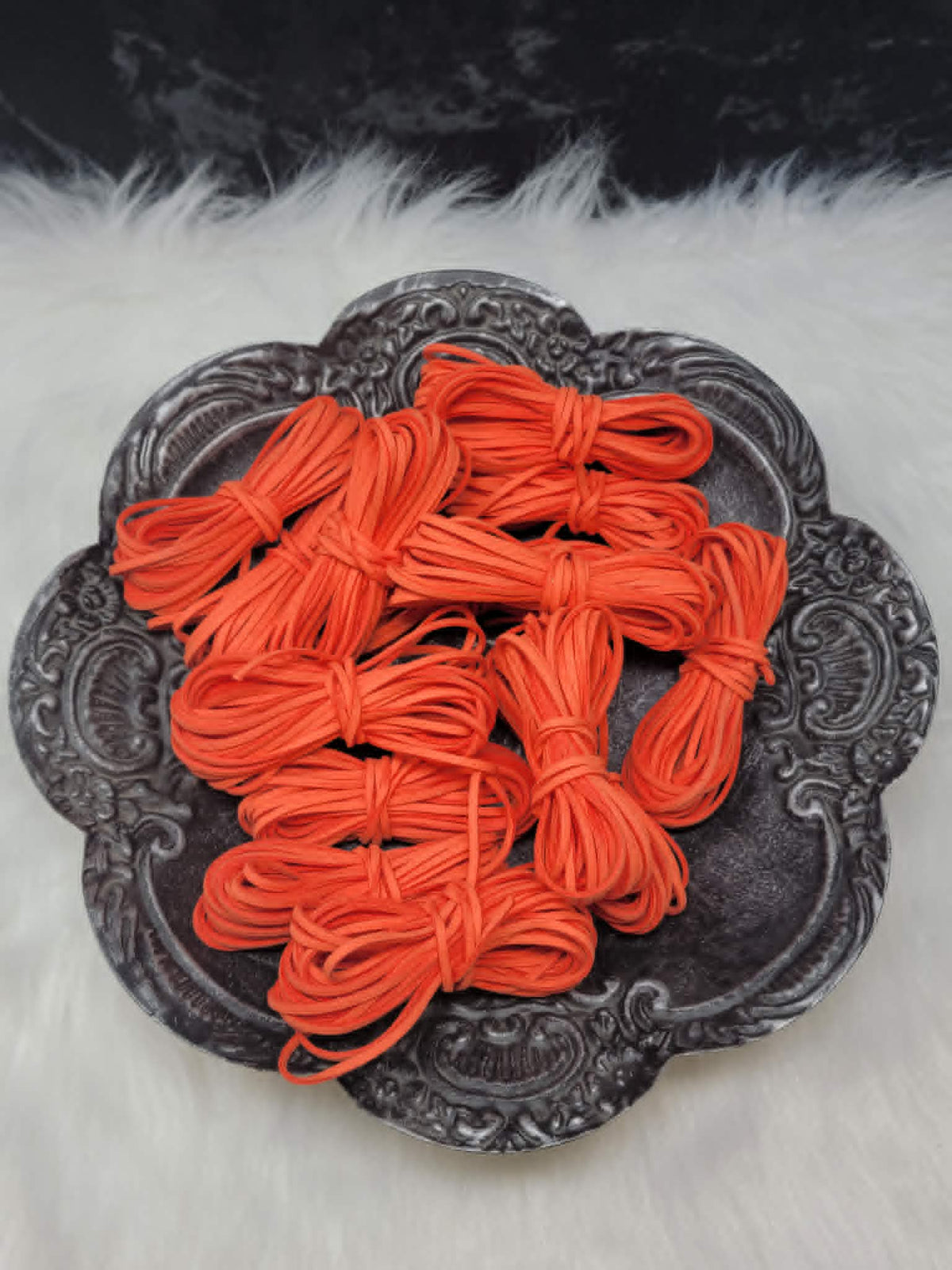 Bundles of 2.7mm tangerine suede leather lacing coiled on a dark scalloped dish