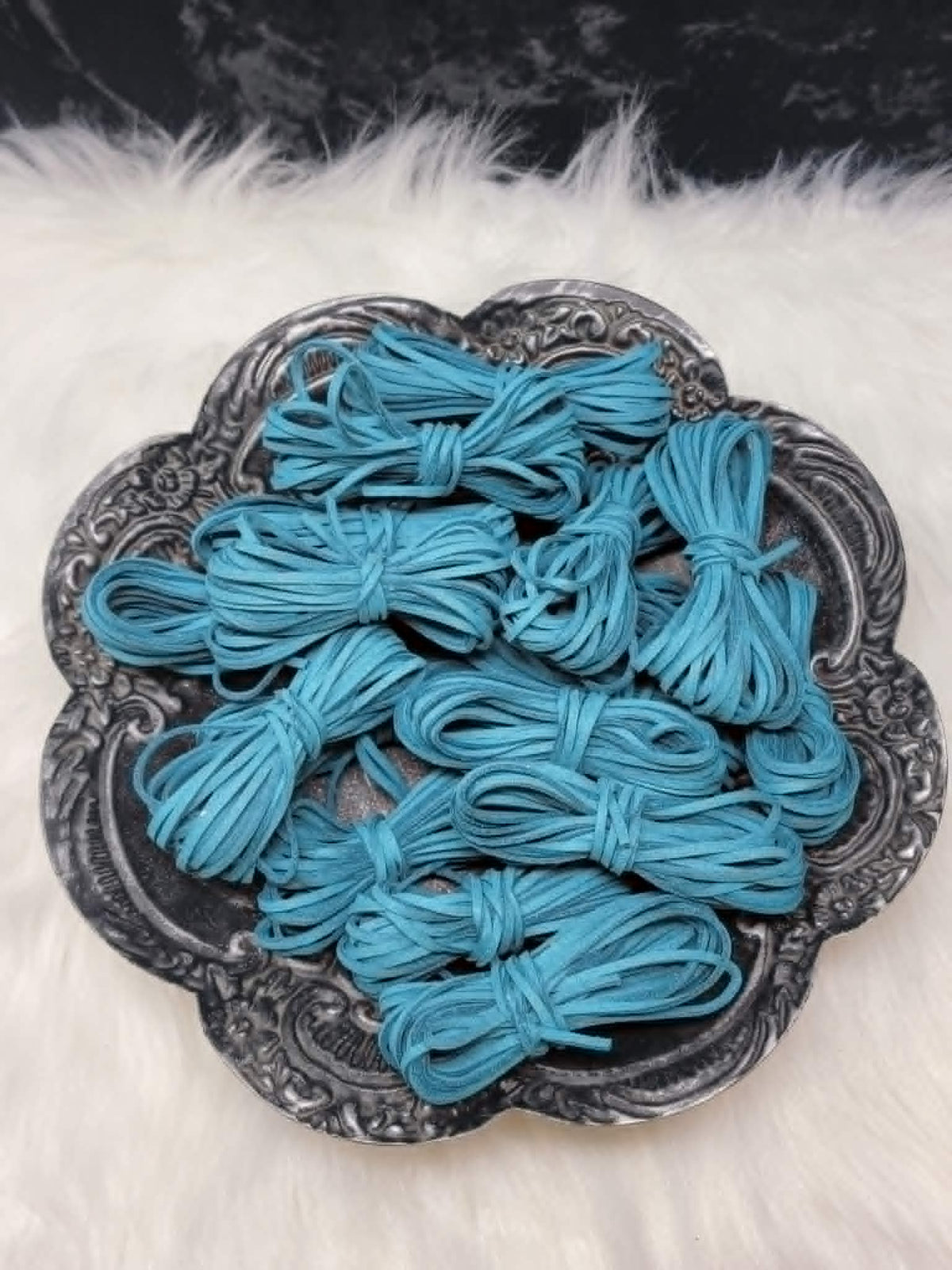Bundles of 2.7mm teal suede leather lacing coiled on a dark scalloped dish
