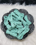 Bundles of 2.7mm turquoise suede leather lacing coiled on a dark scalloped dish