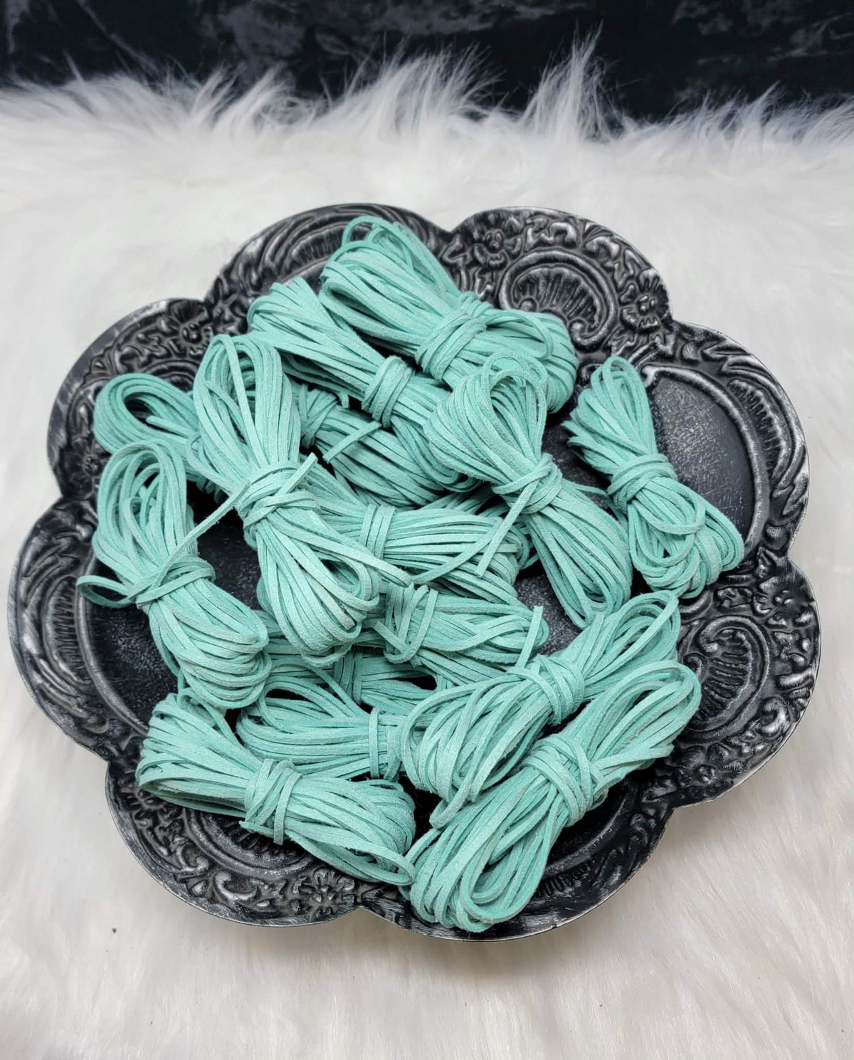 Bundles of 2.7mm turquoise suede leather lacing coiled on a dark scalloped dish