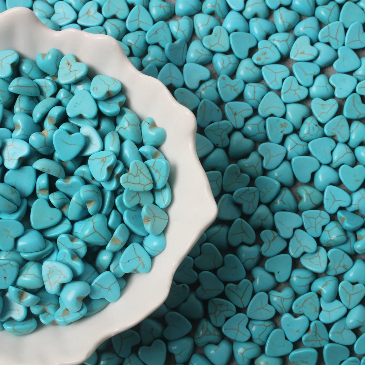 Bowl and pile of 10 x 14mm dyed howlite turquoise heart cabochons (cabs) with natural veining