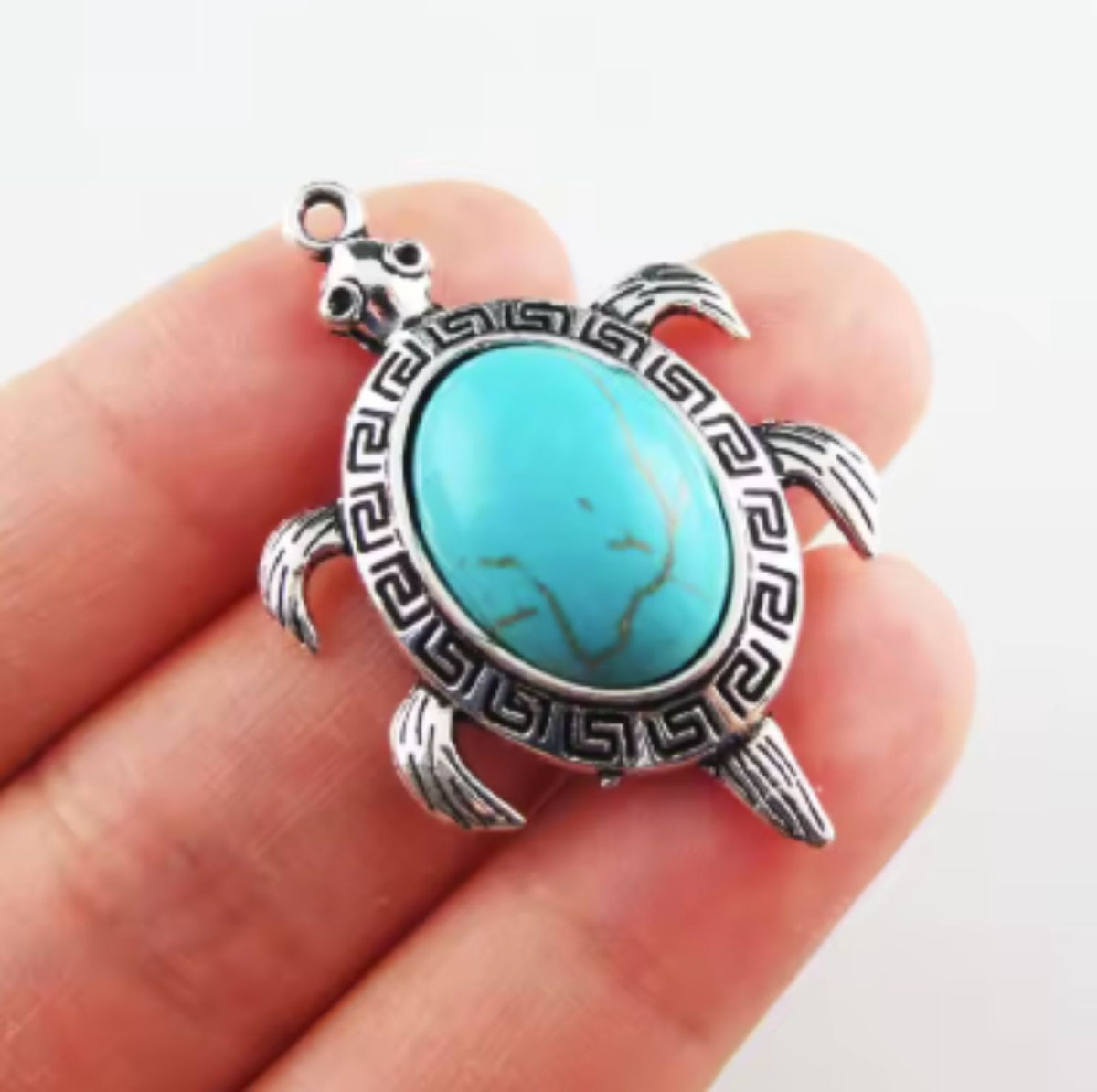 Silver-tone 28 x 42mm turtle pendant with an oval turquoise stone, held in fingers