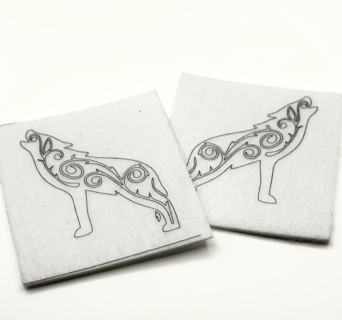 Two beading patterns printed in black on stiff white pellon squares, showing a howling wolf with swirls
