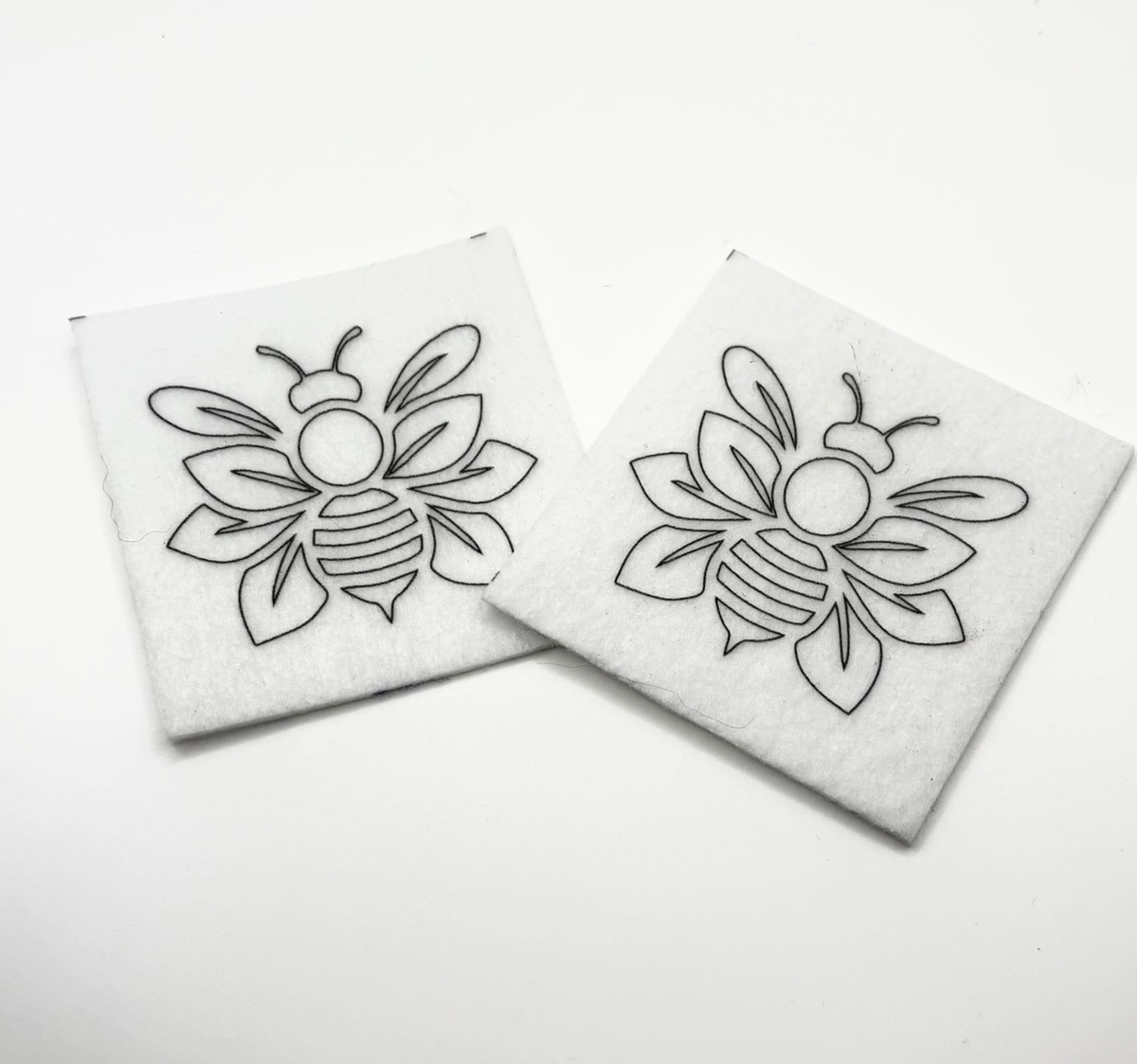 Two beading patterns printed in black on stiff white pellon squares, showing a outlined bee with layered wings