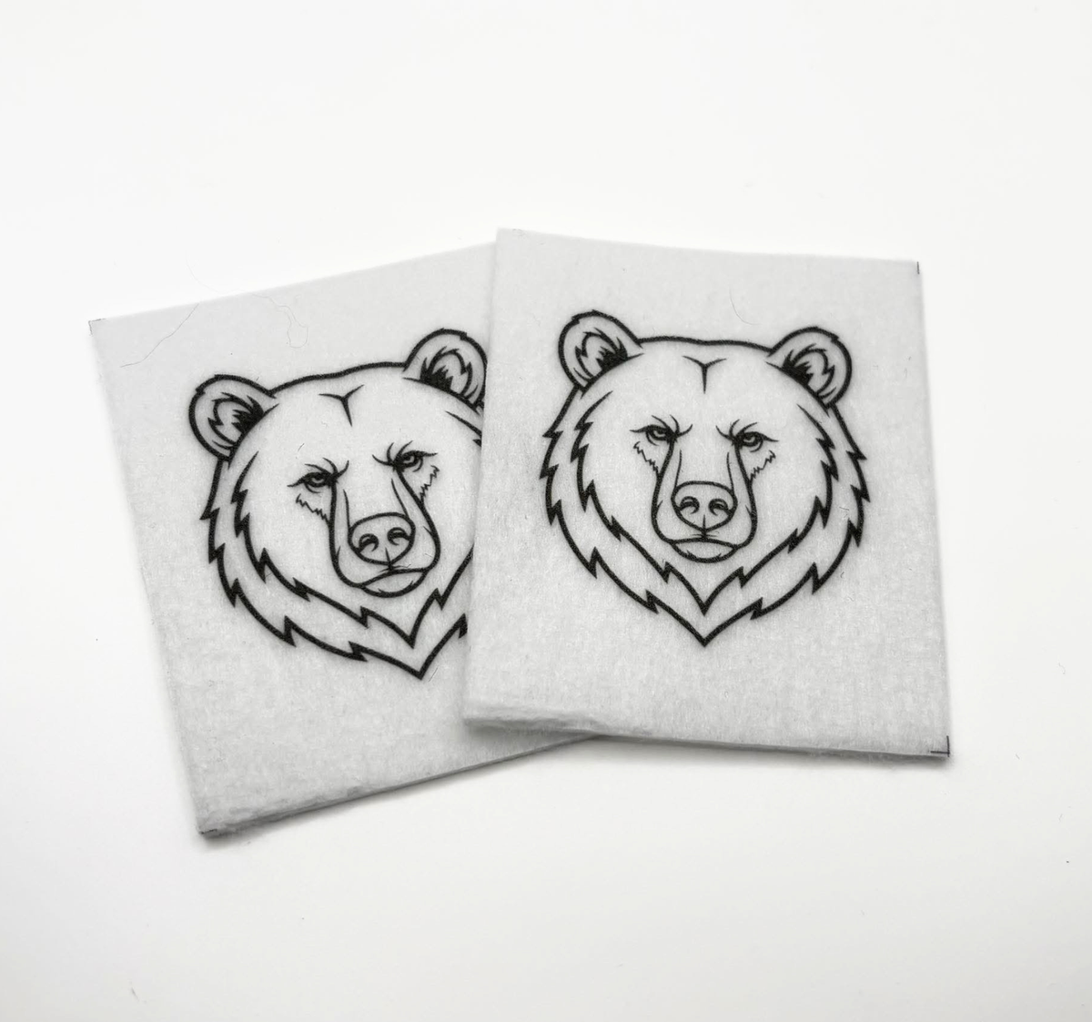 Two beading patterns printed in black on stiff white pellon squares, showing a bear head