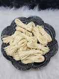 Bundles of 2.7mm vanilla suede leather lacing coiled on a dark scalloped dish