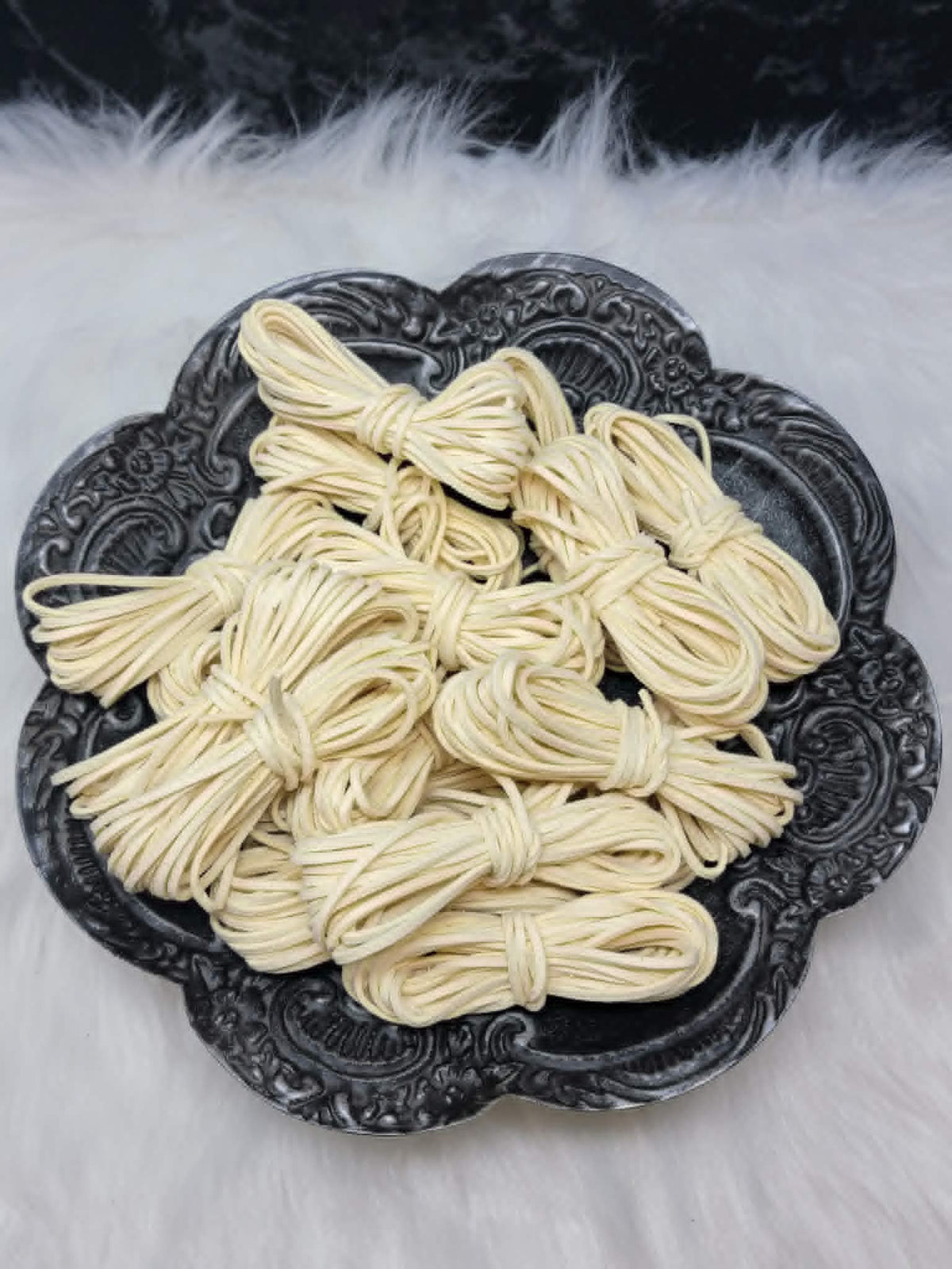 Bundles of 2.7mm vanilla suede leather lacing coiled on a dark scalloped dish