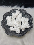 Bundles of 2.7mm white suede leather lacing coiled on a dark scalloped dish