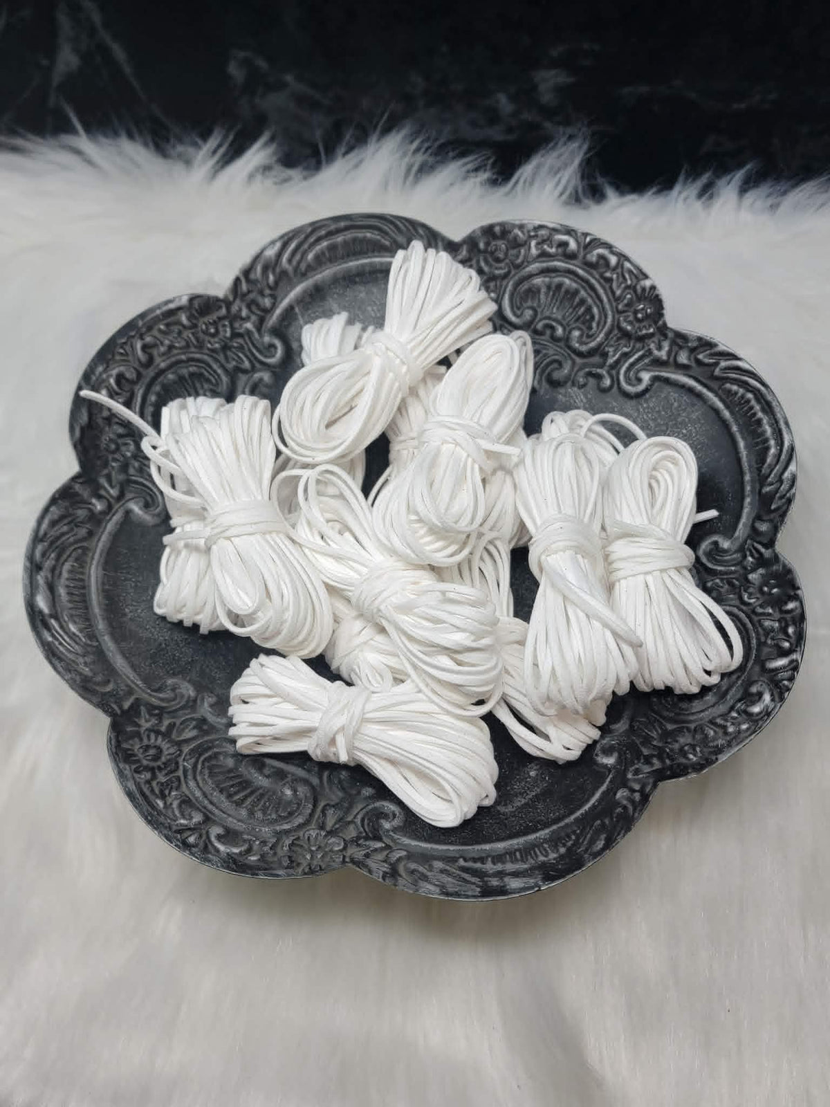 Bundles of 2.7mm white suede leather lacing coiled on a dark scalloped dish