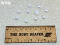 Ten 10mm white pearl-look resin half round cabochons (cabs) beside a ruler