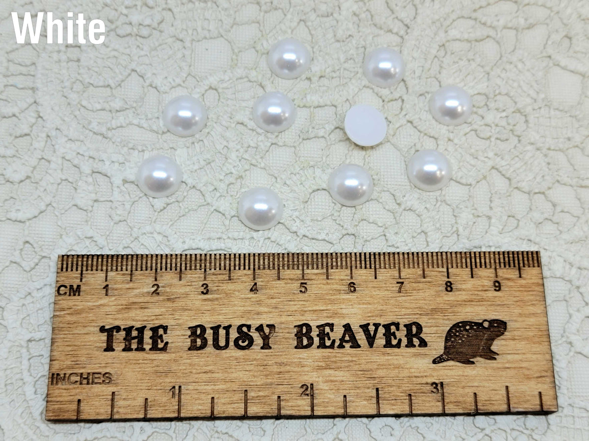Ten 10mm white pearl-look resin half round cabochons (cabs) beside a ruler