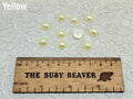 Ten 10mm yellow pearl-look resin half round cabochons (cabs) beside a ruler