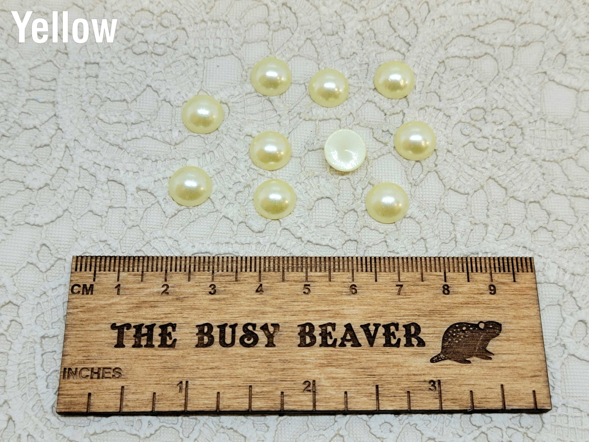 Ten 10mm yellow pearl-look resin half round cabochons (cabs) beside a ruler