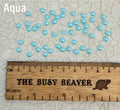 Fifty 5mm aqua pearl-look resin half round cabochons (cabs) scattered beside a ruler