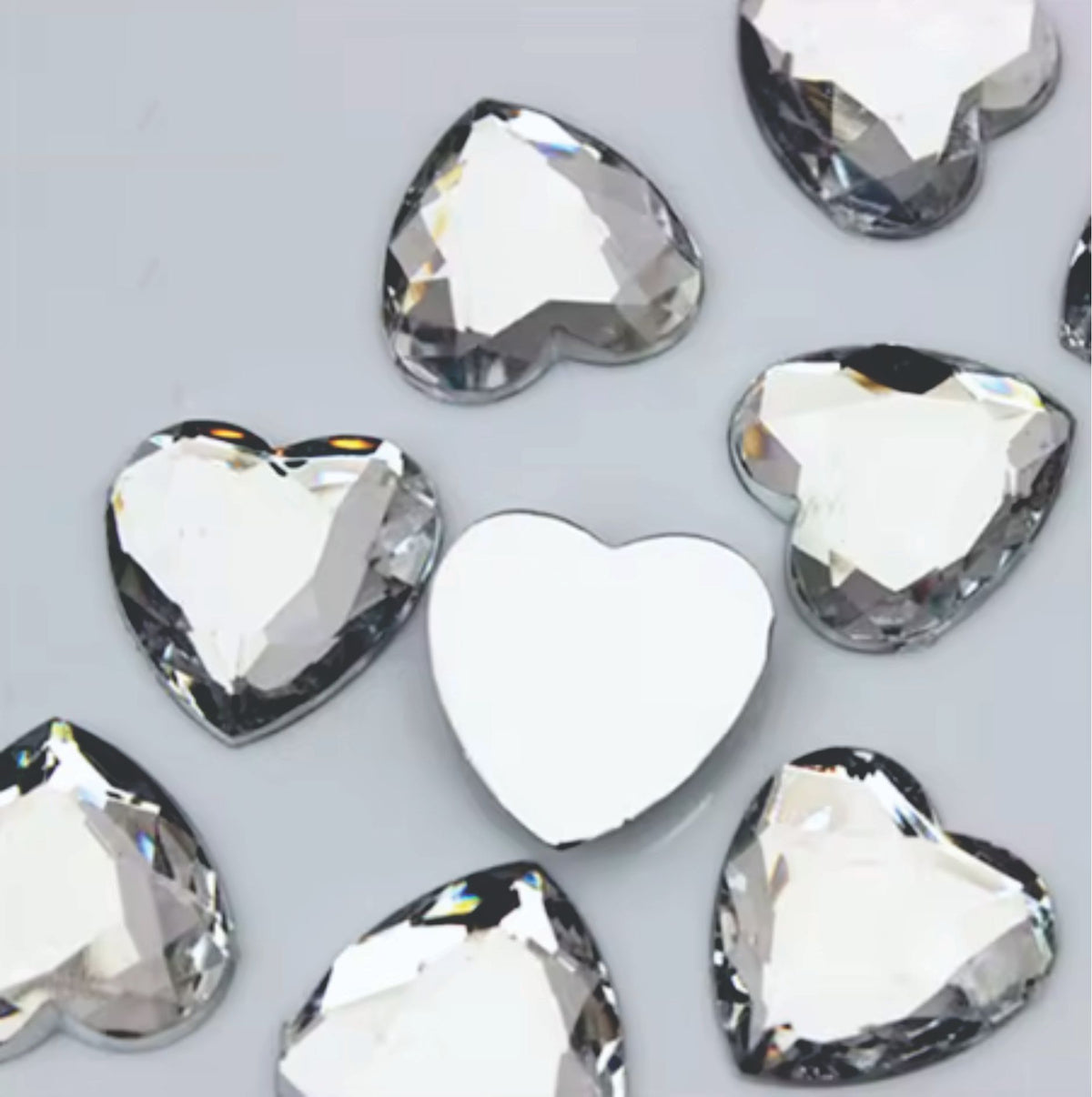 Pile of 20mm faceted crystal resin heart gem cabochons (cabs), one flipped to show the flat back