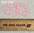 Fifty 5mm dark pink pearl-look resin half round cabochons (cabs) scattered beside a ruler