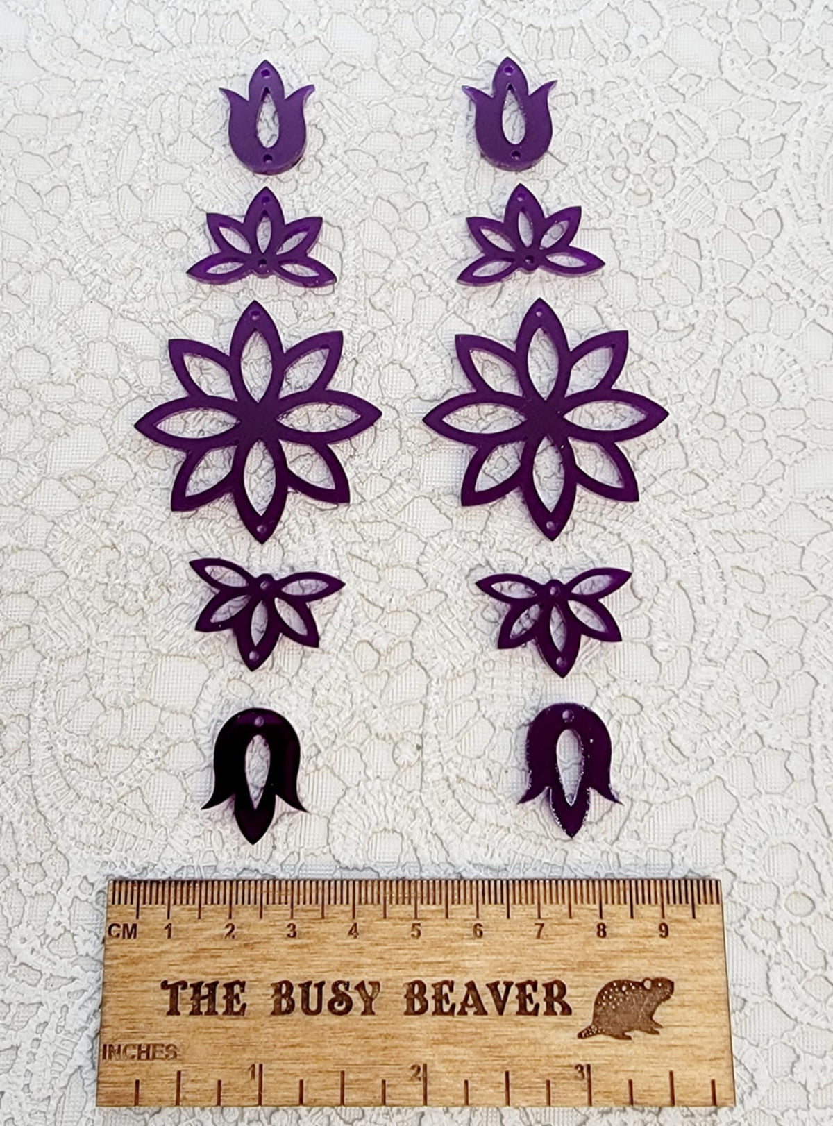 Two 5-tier acrylic flower earring sets in deep purple, laid out top to bottom beside a ruler