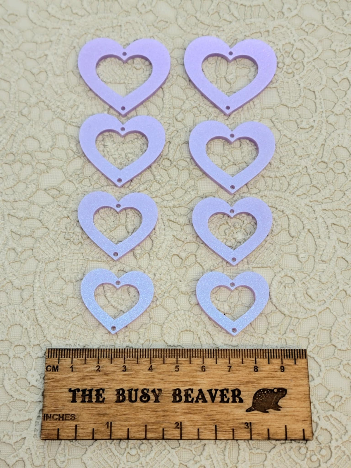 Two sets of four graduated acrylic open hearts in iridescent light purple, beside a ruler