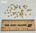 Fifty 5mm gold pearl-look resin half round cabochons (cabs) scattered beside a ruler