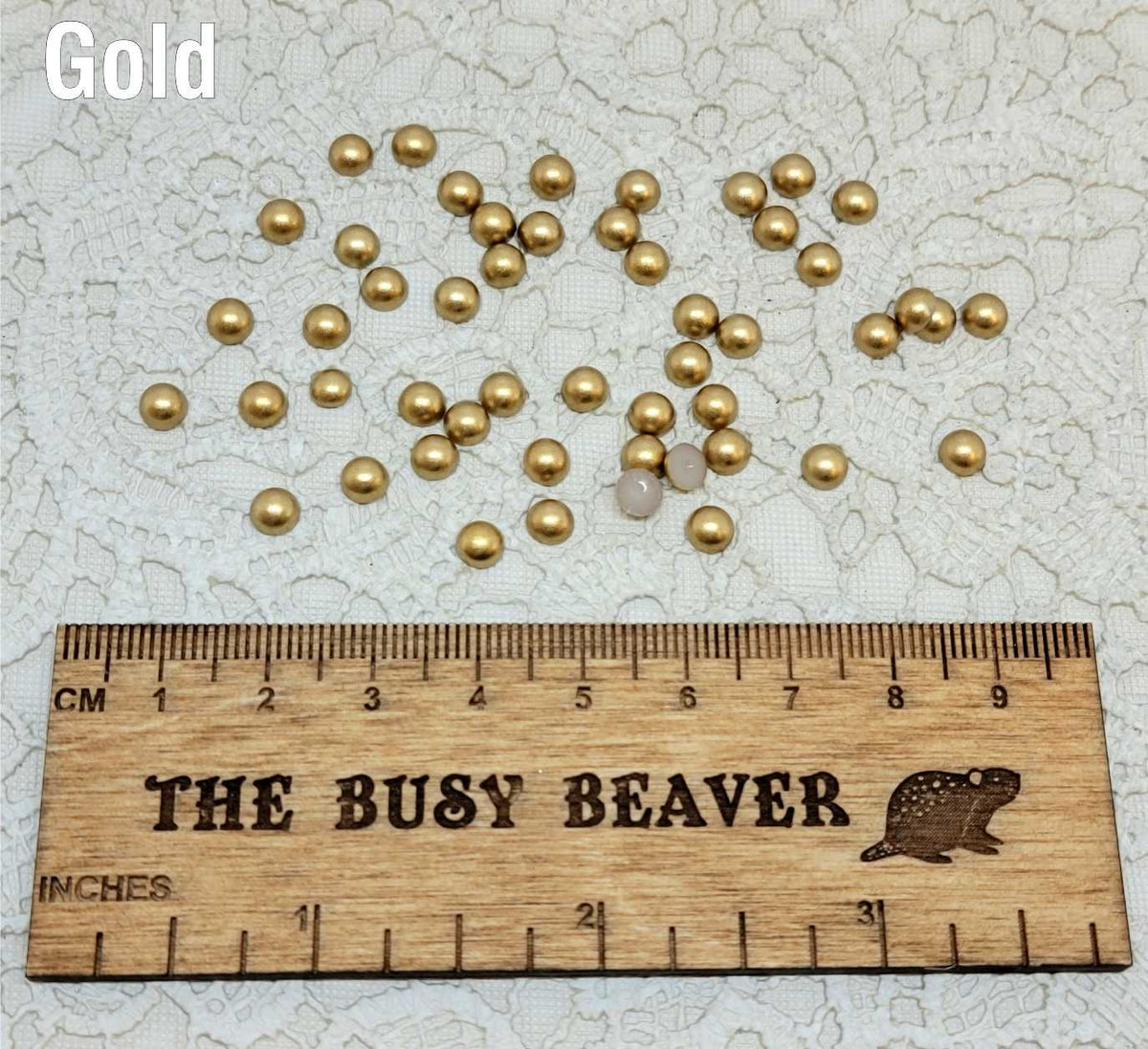 Fifty 5mm gold pearl-look resin half round cabochons (cabs) scattered beside a ruler