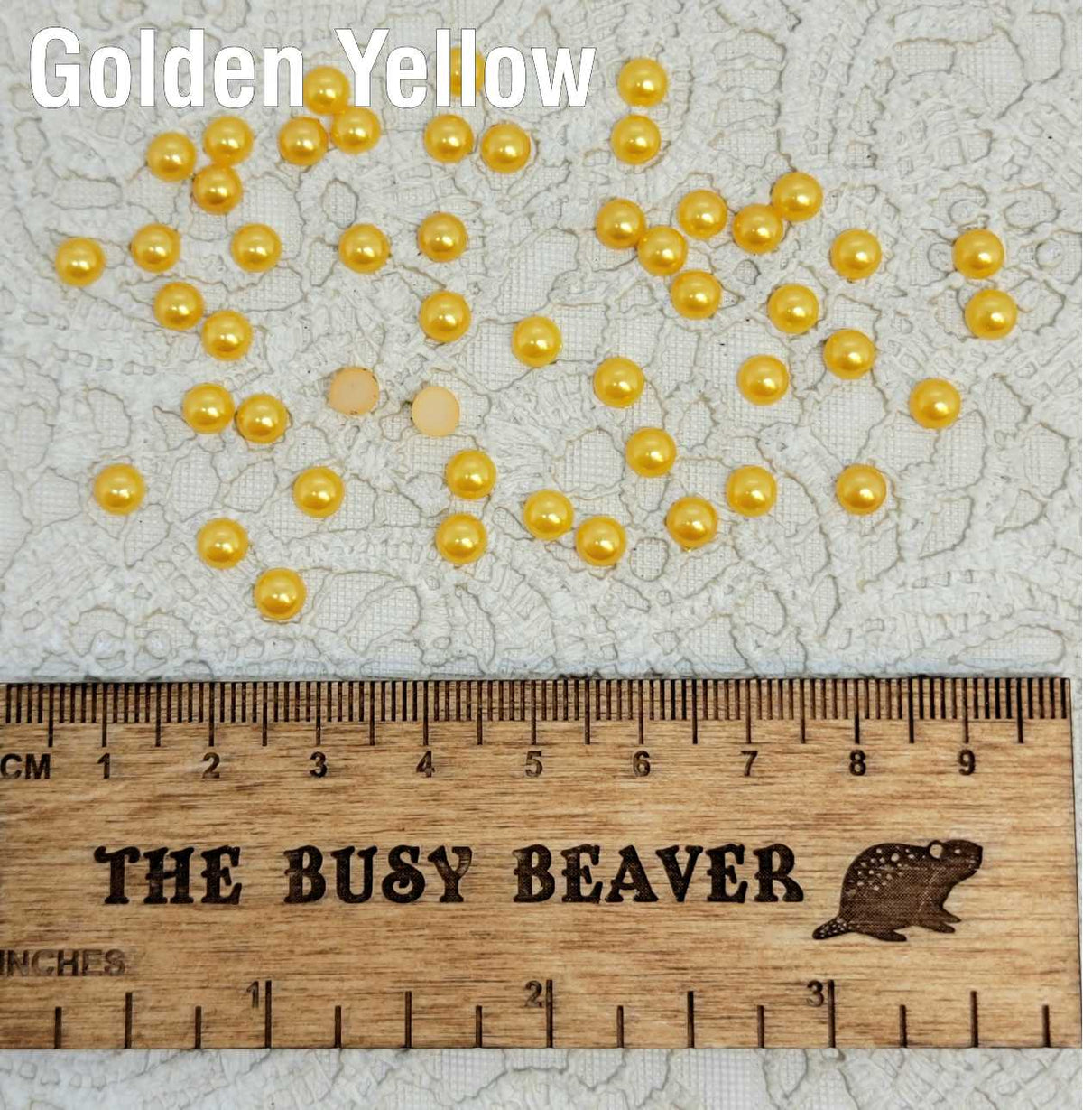 Fifty 5mm golden yellow pearl-look resin half round cabochons (cabs) scattered beside a ruler