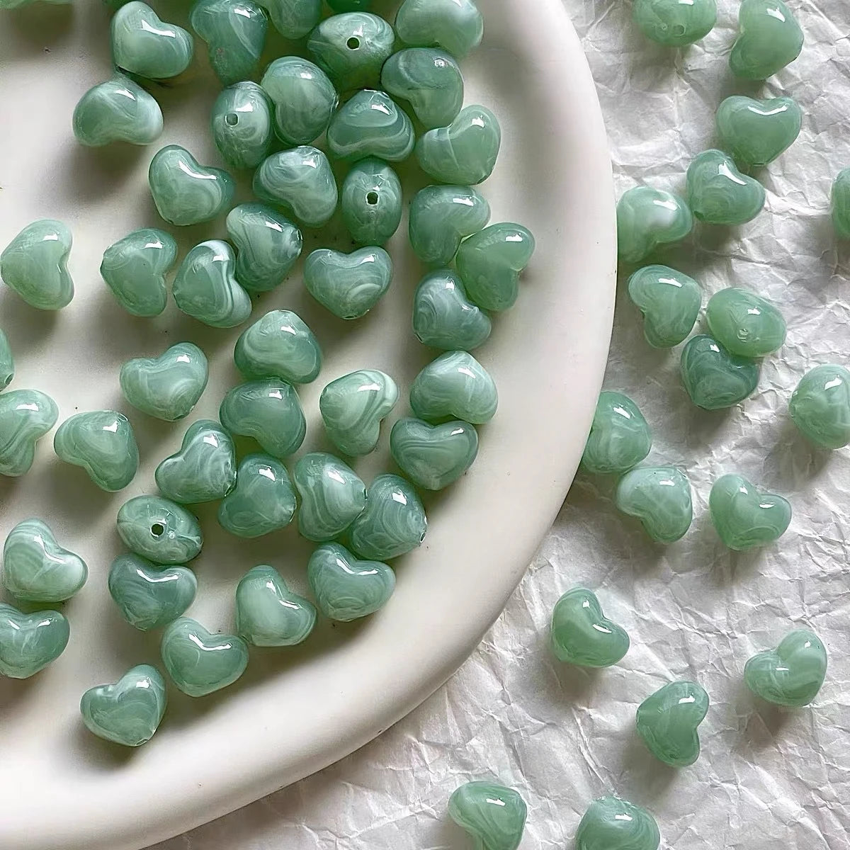 Bowl of 10 x 12mm green swirl heart acrylic beads with a marbled clear finish