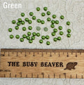 Fifty 5mm green pearl-look resin half round cabochons (cabs) scattered beside a ruler