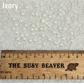 Fifty 5mm ivory pearl-look resin half round cabochons (cabs) scattered beside a ruler