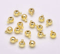 Pile of KC gold stopper crimp beads with loops on a pale background