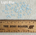 Fifty 5mm light blue pearl-look resin half round cabochons (cabs) scattered beside a ruler
