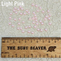 Fifty 5mm light pink pearl-look resin half round cabochons (cabs) scattered beside a ruler