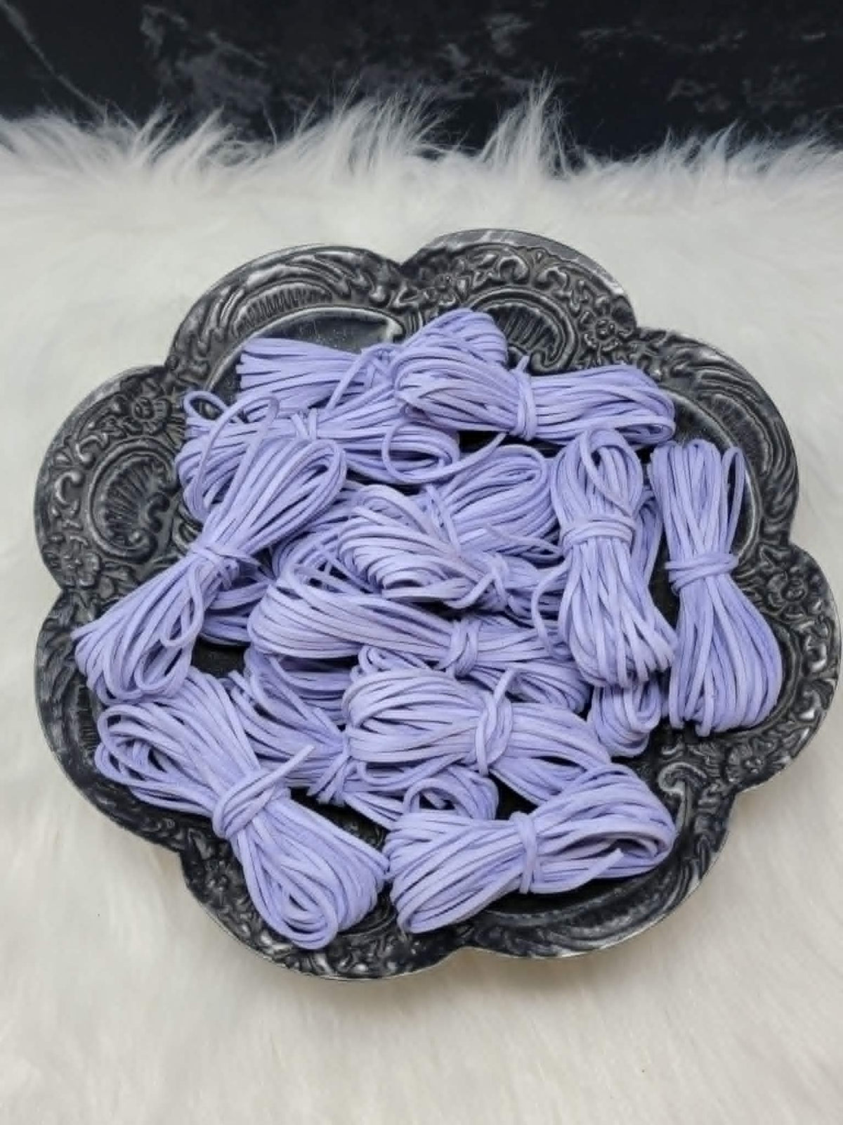 Bundles of 2.7mm periwinkle suede leather lacing coiled on a dark scalloped dish