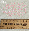 Fifty 5mm pink pearl-look resin half round cabochons (cabs) scattered beside a ruler
