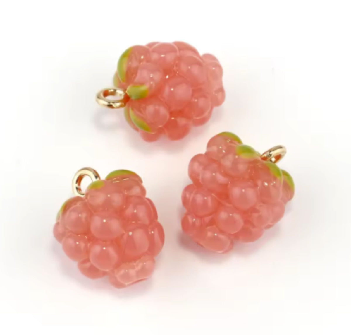 Close-up of two pink resin berry charms with green tops and gold-tone loops